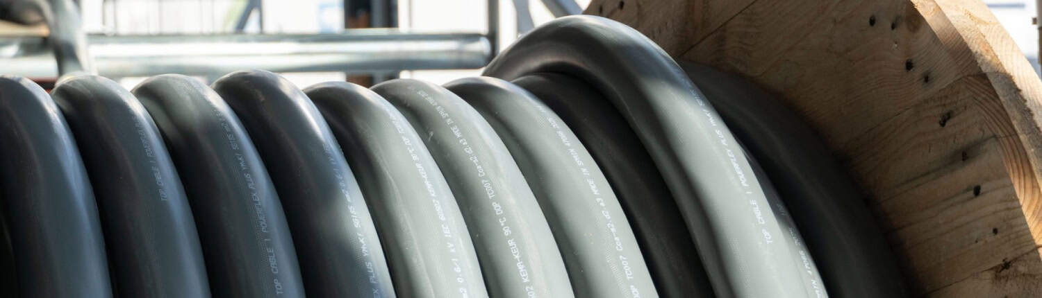 DEKOKabel-02241 Een grote industriële kabel is opgerold rond een houten spoel in een gebouw met grote ramen en een metalen geraamte. Dit laat zien hoe zelfs robuuste materialen kunnen inspireren tot unieke ontwerpelementen voor in huis.